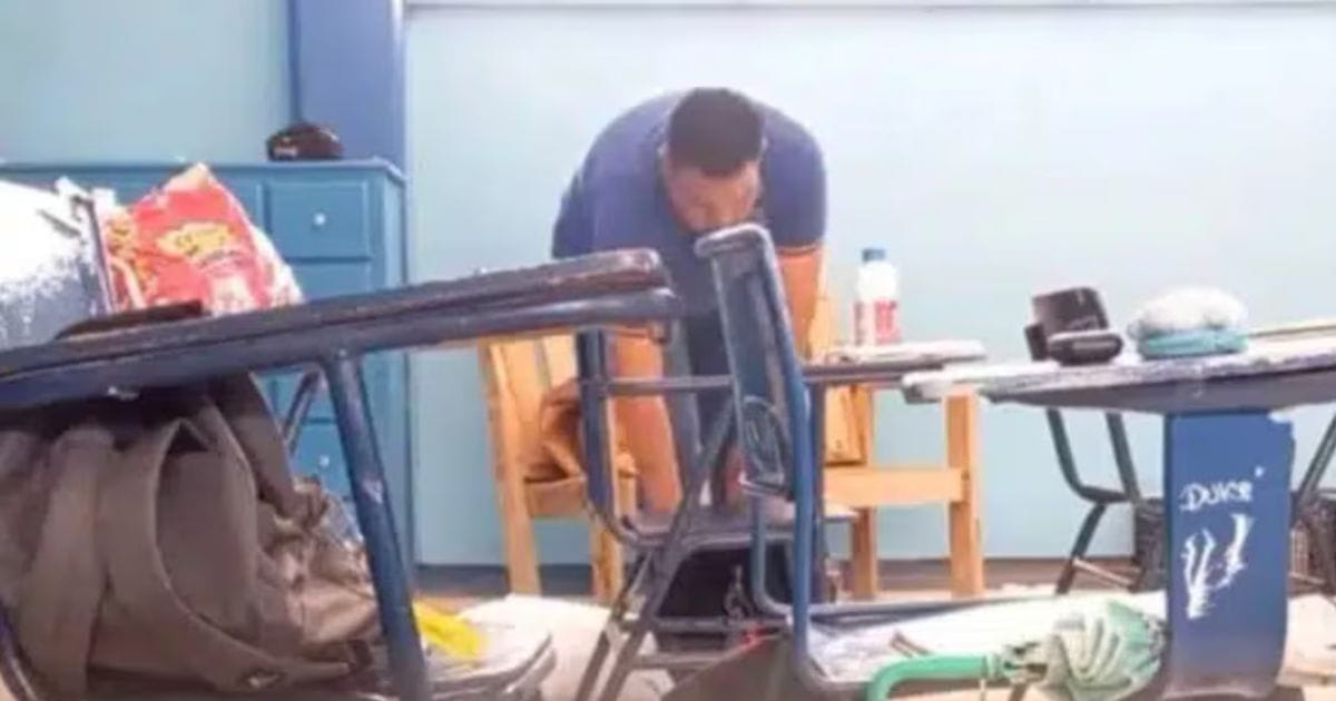 Captura de video de cámara oculta mostrando a un hombre revisando mochilas en un salón de clases